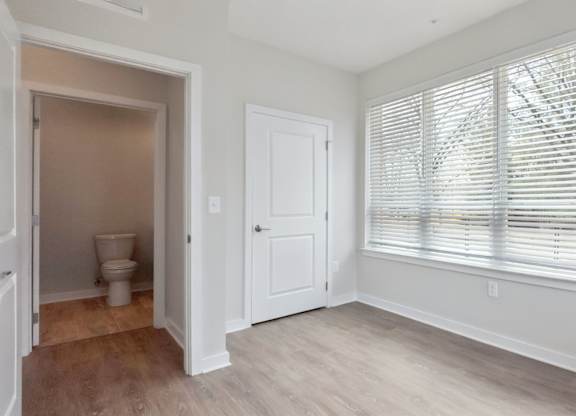 A room with a toilet, a door, and a window with blinds.