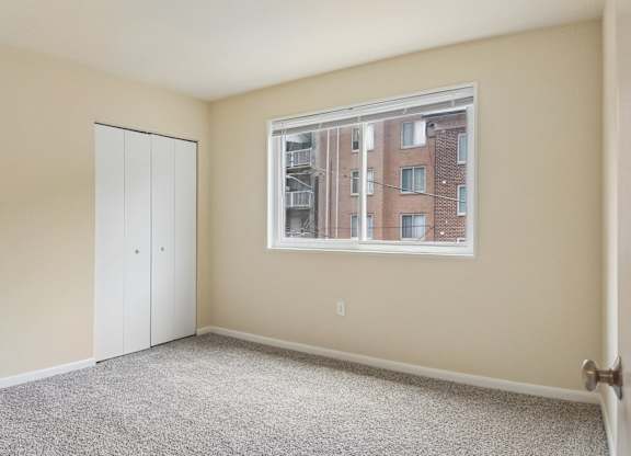 A room with a carpeted floor, a white door, and a window showing a building outside.