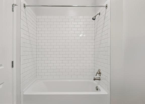A white bathroom with a white tub and white tiles.