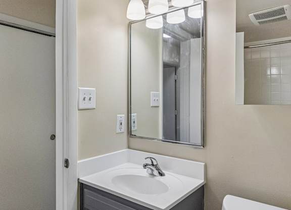 A bathroom with a sink, mirror, and light switches.