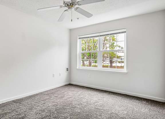 A room with a ceiling fan and a window showing greenery outside.