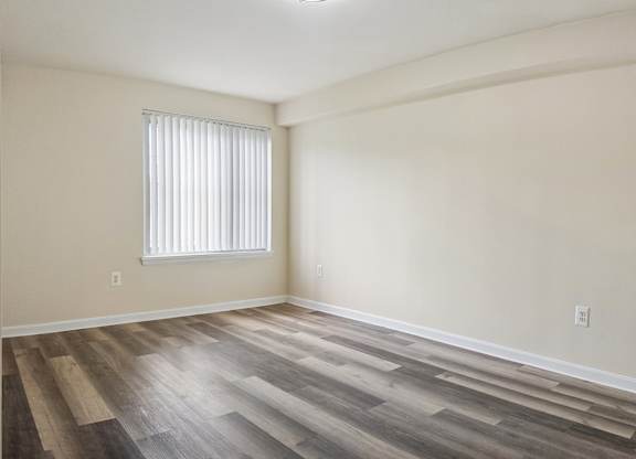A room with wooden flooring and a window with blinds.