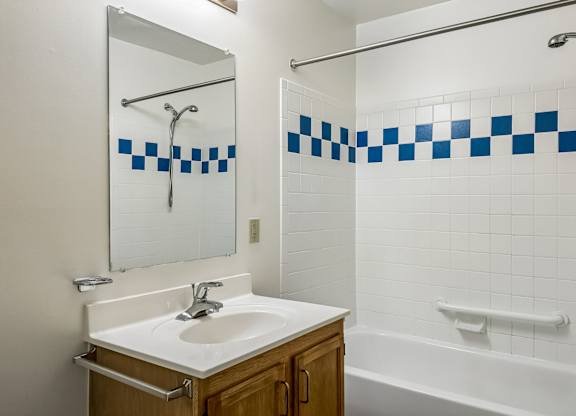 A white sink with a mirror above it and a blue and white tiled shower.