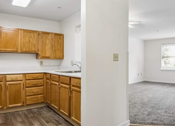 A kitchen with wooden cabinets and a grey carpeted room.
