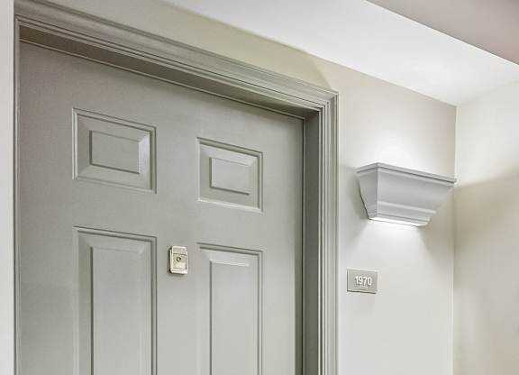 A grey door with a handle and a light switch on the wall.
