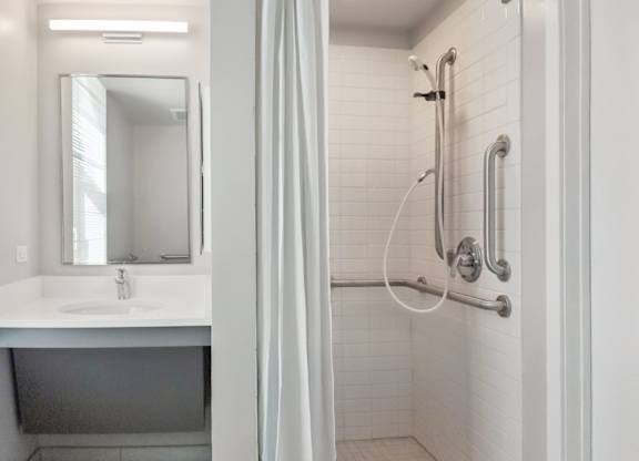 A white bathroom with a sink, mirror, and shower.