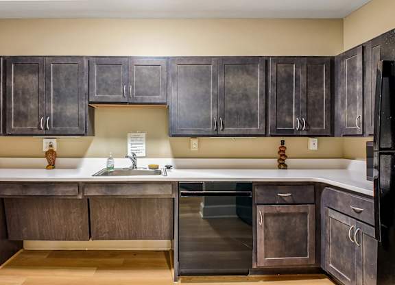 A kitchen with dark wood cabinets and a black refrigerator.