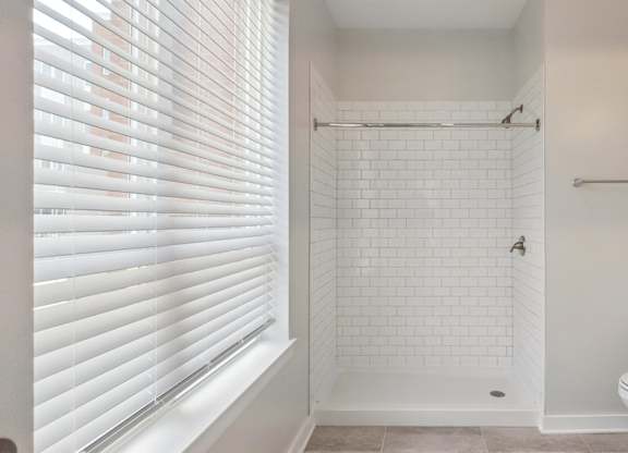A white bathroom with a toilet, sink, and a shower with a white tile wall.
