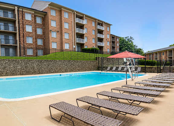 A swimming pool with sun loungers and a red umbrella in front of a brick building.
