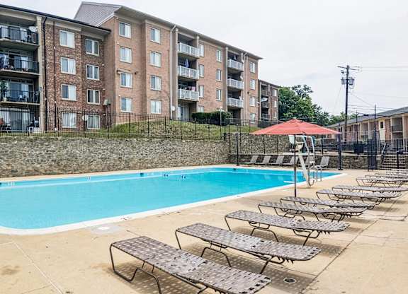 A swimming pool surrounded by sun loungers in front of apartment buildings.