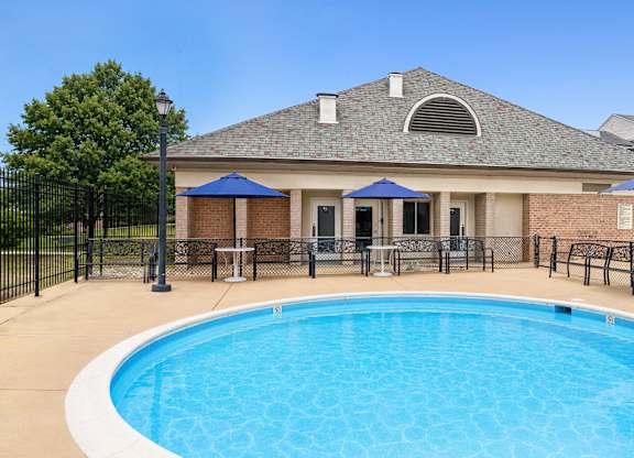 A swimming pool in front of a house with a black fence around it.