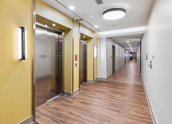 A long hallway with a yellow wall and wood flooring.