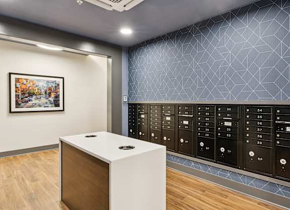 A white reception desk with a black circular object on top is in front of a wall with a framed picture and a row of black lockers.