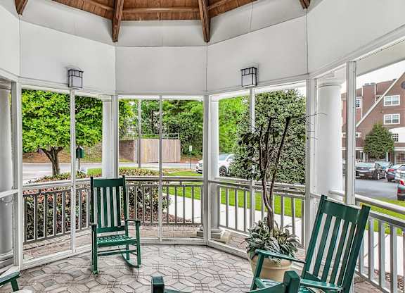 A white gazebo with a wooden roof and a white railing with a green chair and a potted plant.