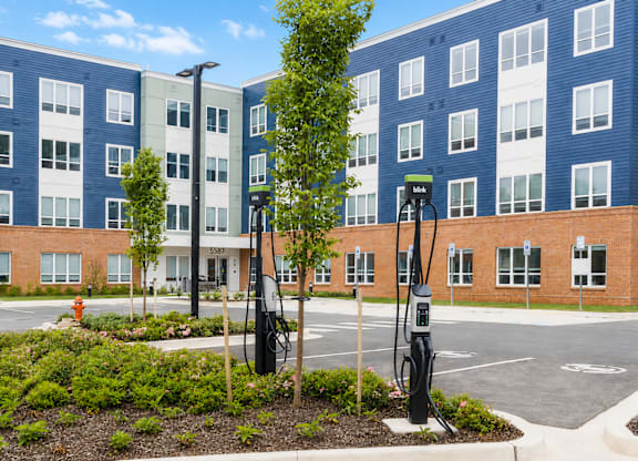 A parking lot with a charging station and a tree in front of a building.