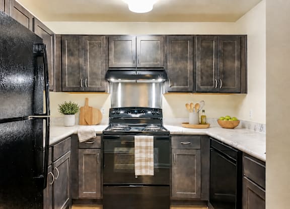 A black refrigerator is in a kitchen with wooden cabinets.