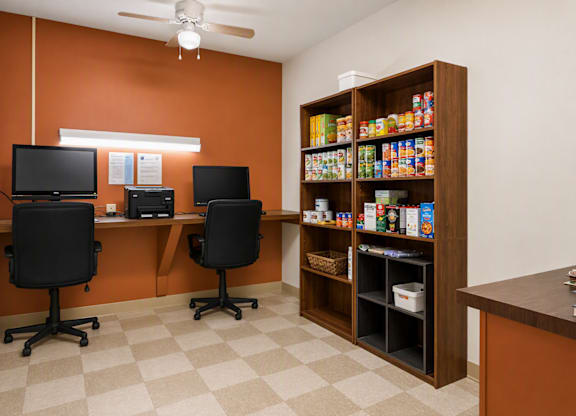 A room with orange walls has two black chairs and a desk with two monitors.