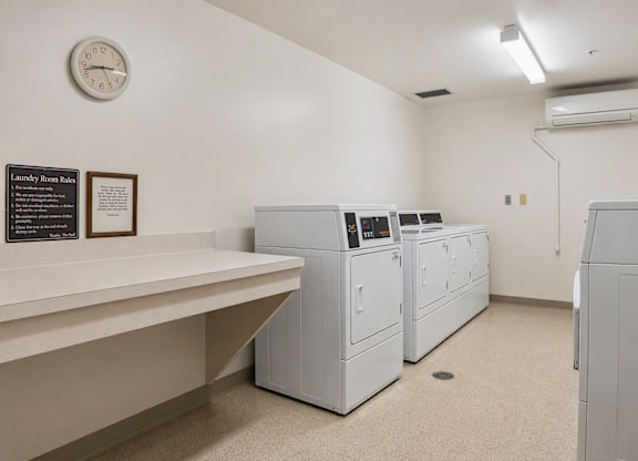 A laundry room with washers and dryers and a clock on the wall.