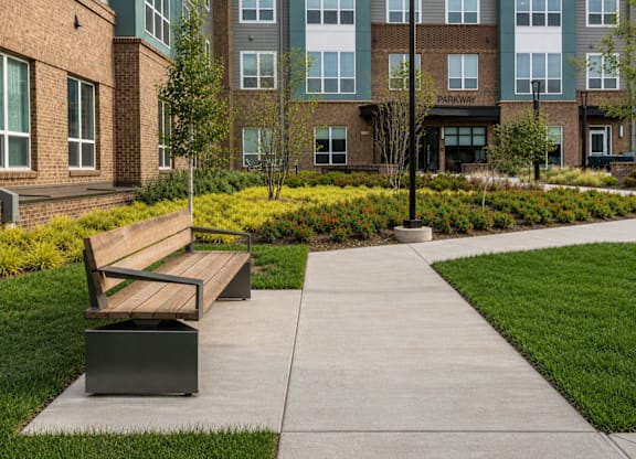 A bench sits on a sidewalk in front of a brick building.