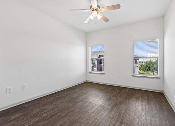 A room with a ceiling fan and two windows.