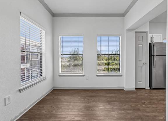 A room with wooden floors and white walls, featuring a refrigerator and a door.