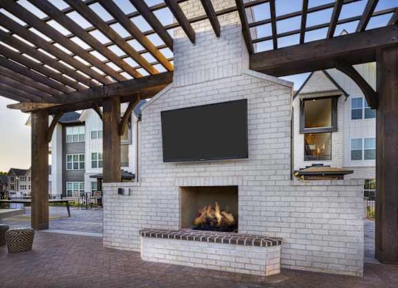 A fireplace with a TV above it is under a wooden pergola at Folksong Apartments, Flowery Branch, Georgia