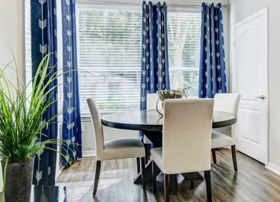 Separate dining area with large windows, window coverings, and a circular wooden table with four cream chairs at Tuscany Bay Apartments, Florida