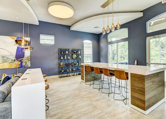 Resident Lounge with oversized windows, pendant lighting, and a stone table with seating at Tuscany Bay Apartments, Tampa, Florida