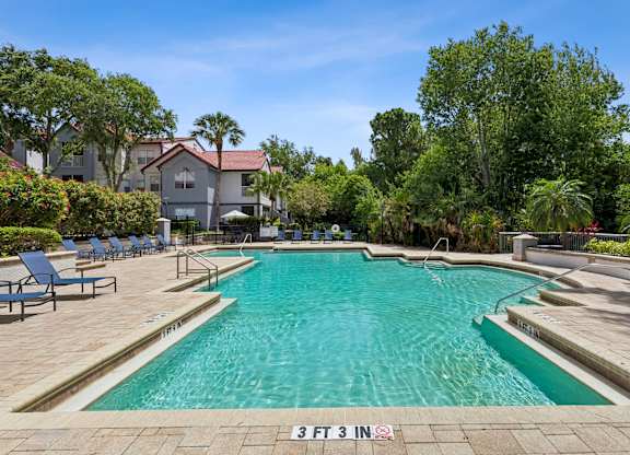 A swimming pool surrounded by trees and chairs.