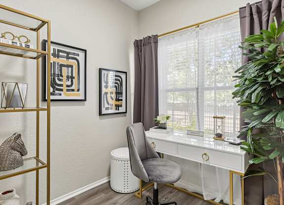 A room with a white desk, a grey chair, and a gold shelf with various objects on it.