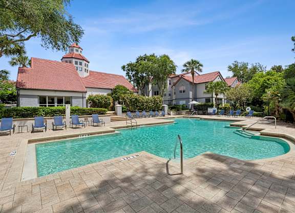 A large swimming pool surrounded by a brick patio and lounge chairs.