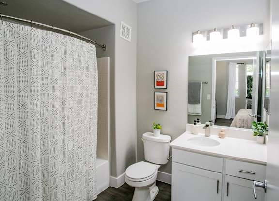 A white bathroom with a toilet, sink, and shower curtain. at Octave Apartments, Nevada