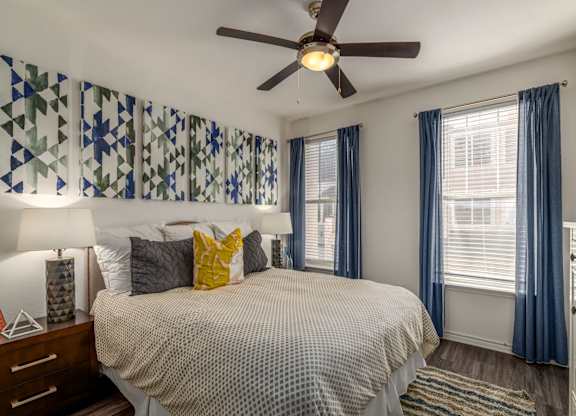 A bedroom with a bed, a ceiling fan, and a window with blue curtains.