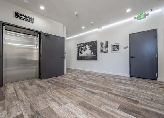 A hallway with a green exit sign and a stainless steel door on the left.