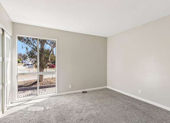 A room with a carpeted floor and a window with a view of a street.