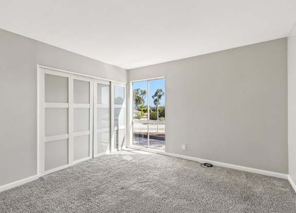 A room with a carpeted floor and a view of the outside through a glass door.