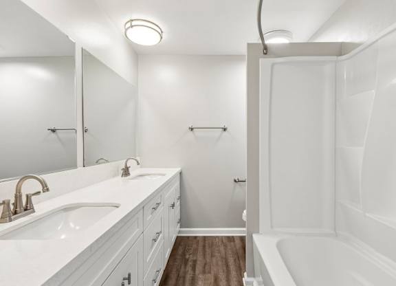 A white bathroom with a sink, mirror, and tub.