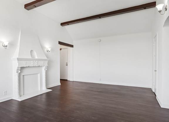 A room with a white fireplace and wooden beams on the ceiling.