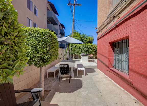 A patio with a table and chairs is surrounded by a brick wall and a green bush.