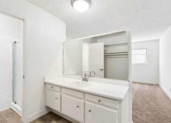 A white bathroom with a sink, mirror, and cabinets.