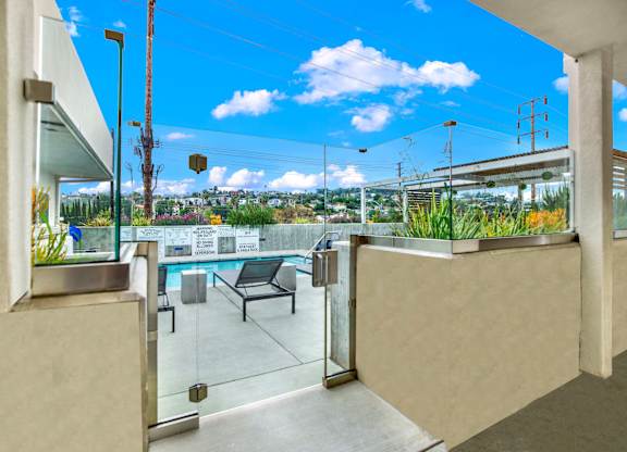 A balcony with a glass door and a bench overlooking a pool.