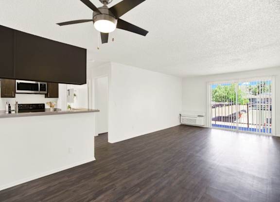 A room with a ceiling fan and a kitchen area with white cabinets at Monterra Ridge Apartments, Canyon Country