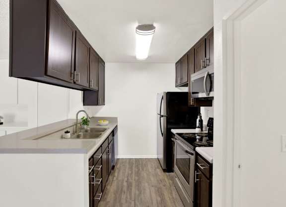 A kitchen with dark brown cabinets and white appliances at Monterra Ridge Apartments, Canyon Country