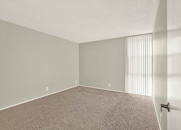 A room with a carpeted floor and a door on the right side at The Square in Downey, CA, 90242