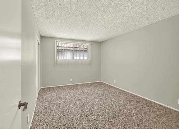 A room with a carpeted floor and a window with blinds at The Square in Downey, CA, 90242