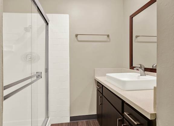 A bathroom with a sink, mirror, and shower at The Square in Downey, CA, 90242
