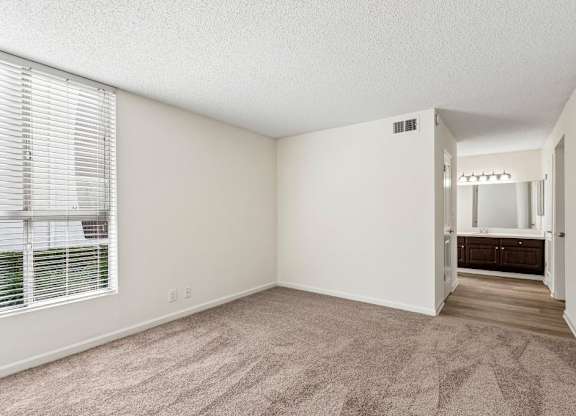 A room with a carpeted floor and a window with blinds.