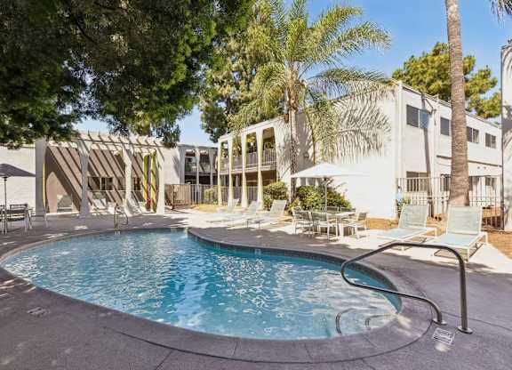 A swimming pool surrounded by lounge chairs and umbrellas in a residential area.
