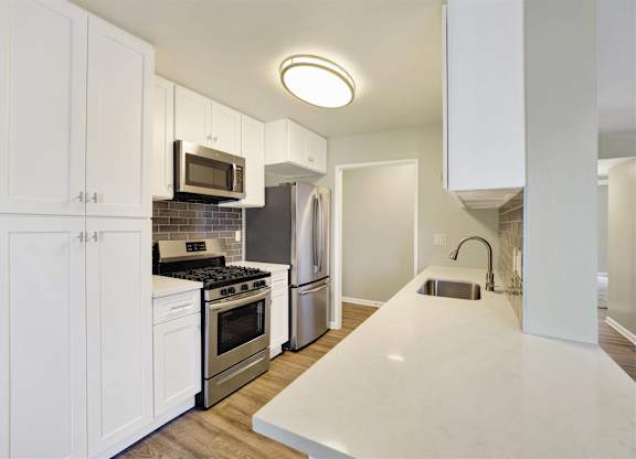 White galley kitchen with peninsula and stainless steel appliances at Parc @ 5 Apartments, Downey, 90240