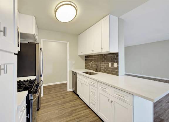 Galley kitchen with white countertops and modern fixtures at Parc @ 5 Apartments, Downey, California